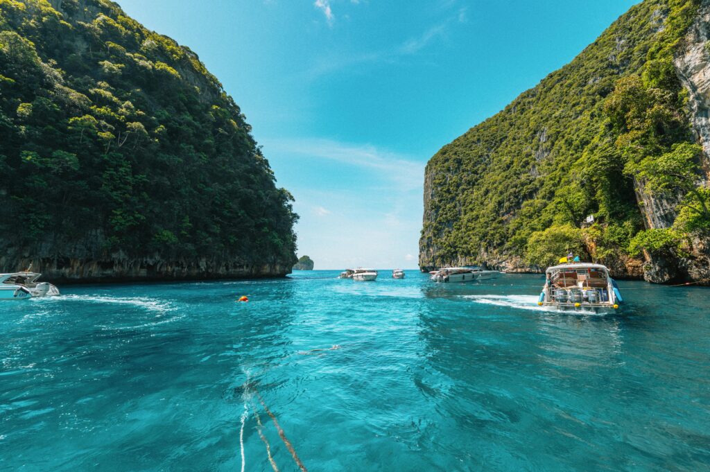 Explore the clear waters and lush cliffs of Krabi, Thailand, with boats navigating between stunning formations.